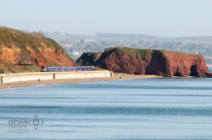 Looking across the sea towards the Dawlish coastline with a First Great Western train on the sea wall